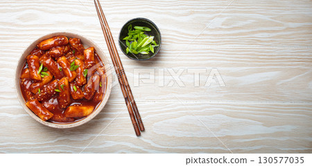 Traditional Korean tteokbokki served in white bowl with chopsticks and sesame seeds on white wooden rustic background, space for text 130577035