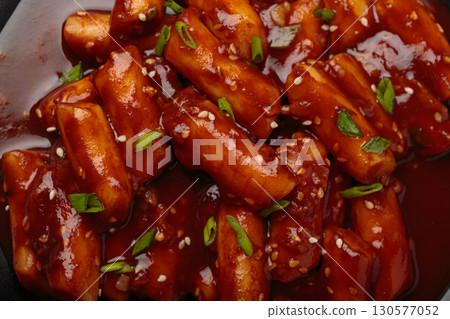 Close up of traditional Korean tteokbokki served with sesame seeds on black rustic background Close up of traditional Korean tteokbokki served with sesame seeds on black rustic background 130577052