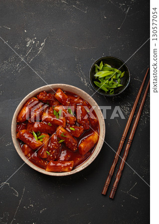 Traditional Korean tteokbokki served on white plate with chopsticks and sesame seeds on black rustic background 130577054