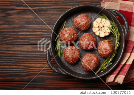 Raw meatballs with garlic and rosemary in cast iron pan on wooden background, space for text 130577055