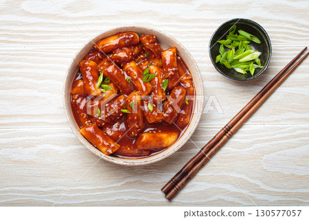 Traditional Korean tteokbokki served in white bowl with chopsticks and sesame seeds on white wooden rustic background 130577057