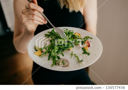 Woman holding plate filled with vibrant, fresh salad featuring arugula, cucumber, peach, and cheese, savoring flavors while embracing healthy lifestyle and nutritious eating habits. Wellness nutrition Woman holding plate filled with vibrant, fresh salad featuring arugula, cucumber, peach, and cheese, savoring flavors while embracing healthy lifestyle and nutritious eating habits. Wellness nutrition 130577436
