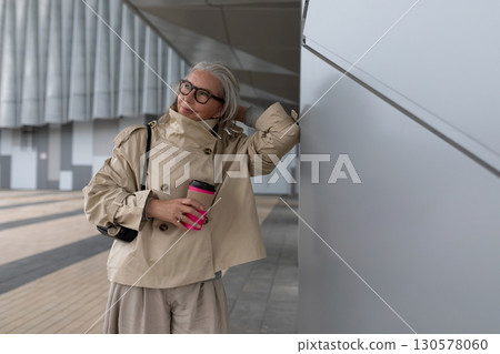 Confident woman in stylish trench coat enjoying coffee in urban setting during comfortable weather Confident woman in stylish trench coat enjoying coffee in urban setting during comfortable weather 130578060