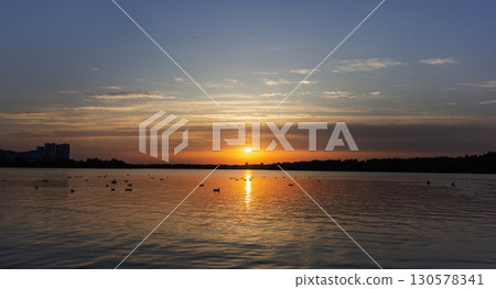 Bright sky at sunset, light clouds, lake, forest, houses Bright sky at sunset, light clouds, lake, forest, houses 130578341