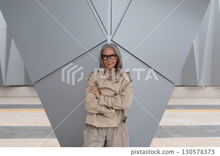 Modern woman poses confidently in urban setting with geometric architecture in the background during 130578373