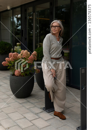 Woman in casual outfit poses confidently outside a modern building surrounded by flowers during a Woman in casual outfit poses confidently outside a modern building surrounded by flowers during a 130578375
