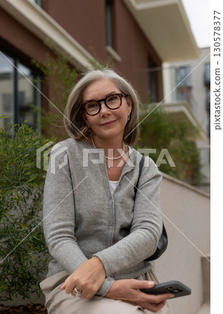 Woman sitting on steps outside a modern building, enjoying a moment of calm in the afternoon sun 130578377