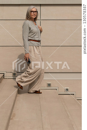 Woman walking gracefully down stone steps in a modern architectural setting during daylight 130578387