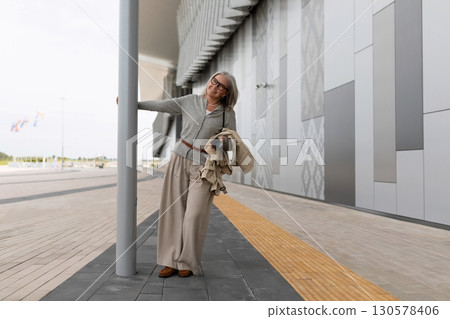 Woman in light attire leans against pole while exploring modern architecture during daylight Woman in light attire leans against pole while exploring modern architecture during daylight 130578406