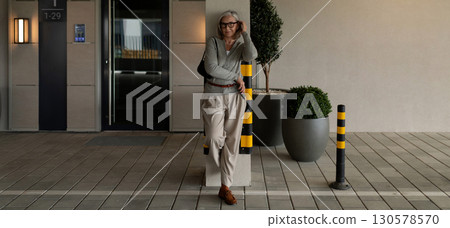Woman casually leaning against a pillar in a modern building lobby during daylight hours 130578570