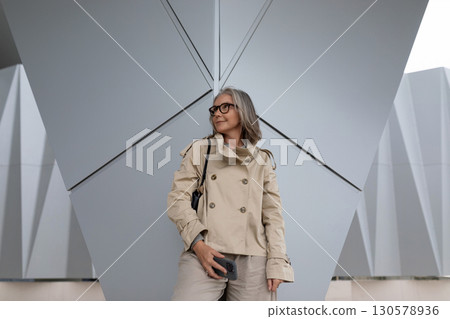 Stylish woman stands confidently in modern architectural setting during daylight, showcasing 130578936