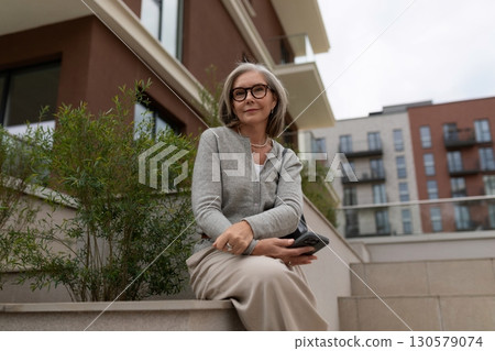 Older woman enjoying a quiet moment on a sunny terrace in the city while holding a smartphone and Older woman enjoying a quiet moment on a sunny terrace in the city while holding a smartphone and 130579074