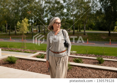 Elegant woman enjoying a sunny day outdoors while wearing stylish attire and posing near landscaped 130579128