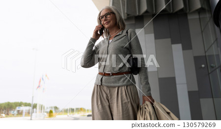 Professional woman talking on phone outside modern building on a cloudy day 130579269