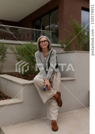 Stylish mature woman relaxing outdoors in a modern urban environment during a sunny day 130579951