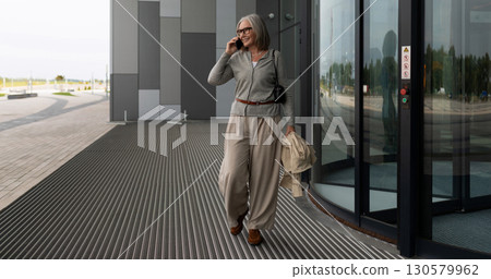 Senior woman enjoying a casual afternoon while talking on her phone outside a contemporary building Senior woman enjoying a casual afternoon while talking on her phone outside a contemporary building 130579962
