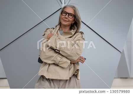 Elegant woman poses confidently in a stylish beige coat against a modern architectural backdrop Elegant woman poses confidently in a stylish beige coat against a modern architectural backdrop 130579980