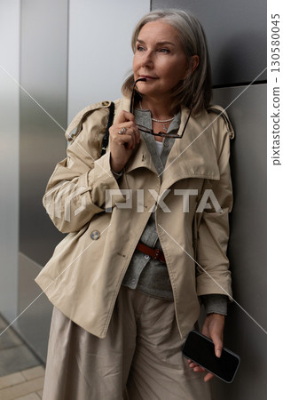 Stylish older woman poses elegantly near modern building in daytime Stylish older woman poses elegantly near modern building in daytime 130580045