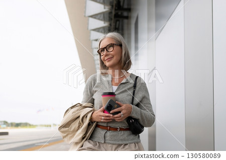 Woman at airport terminal enjoying coffee while waiting for her flight during sunny day 130580089