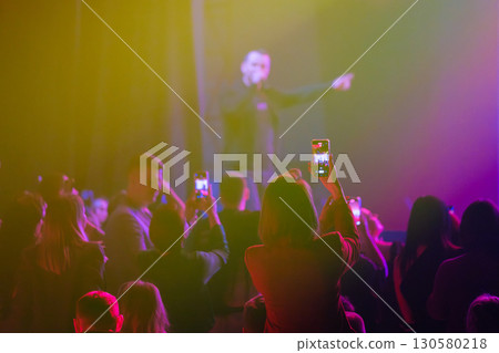 Crowd enjoying a live music performance with colorful stage lighting 130580218