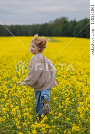 Smiling girl in beige sweater running in yellow flower field looking at camera Smiling girl in beige sweater running in yellow flower field looking at camera 130581061