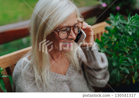 Senior woman standing terrace making phone call. Senior woman standing terrace making phone call. 130581317