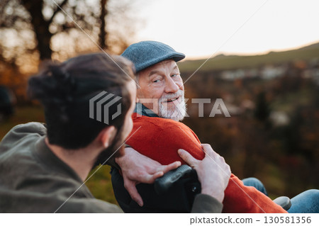 Grandson standing behind his older grandad in wheelchair, enjoying view. 130581356