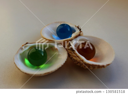 Colored transparent glass beads similar to pearls inside the halves of sea shells 130581518