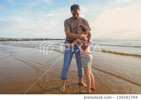 Dad tenderly hugs his happy 8 year old daughter on beach near sea Dad tenderly hugs his happy 8 year old daughter on beach near sea 130581704