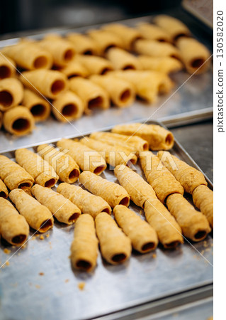 Unbaked puff pastry tubes on tray ready for cream filling in bakery kitchen Unbaked puff pastry tubes on tray ready for cream filling in bakery kitchen 130582020