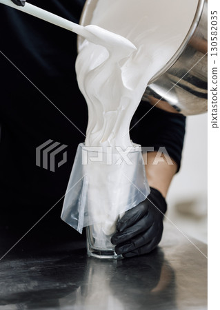 Pouring fluffy meringue into piping bag for pastry preparation in professional kitchen Pouring fluffy meringue into piping bag for pastry preparation in professional kitchen 130582035