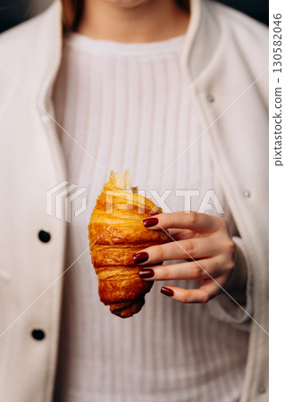 Woman holding buttery croissant in hand, elegant style, minimalist background Woman holding buttery croissant in hand, elegant style, minimalist background 130582046