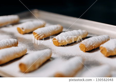 Freshly baked cream rolls sprinkled with powdered sugar on a metal tray in bakery Freshly baked cream rolls sprinkled with powdered sugar on a metal tray in bakery 130582048