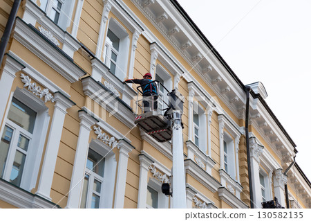 Construction worker on a platform lift cleaning and restoring facade of building. The image captures urban maintenance, safety, and renovation in city environment 130582135