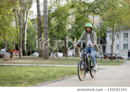 Biker enjoying a sunny day in a city park while riding a mountain bike along a pathway with lush greenery surrounding Biker enjoying a sunny day in a city park while riding a mountain bike along a pathway with lush greenery surrounding 130582163