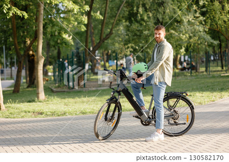 Man enjoys biking in a park on a sunny day while wearing a helmet and smiling at the camera 130582170