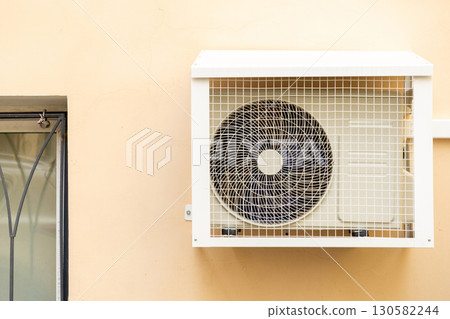 air conditioner in an anti-vandal grid is installed on wall of house.  130582244