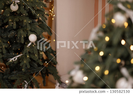 Christmas trees with white baubles and lights in room with beige wall Christmas trees with white baubles and lights in room with beige wall 130582530