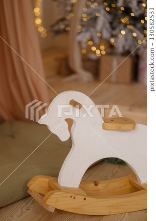 Wooden rocking horse toy on wooden floor near Christmas tree with lights Wooden rocking horse toy on wooden floor near Christmas tree with lights 130582531
