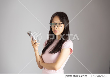 Woman is holding a smartphone and looking directly at the camera. Woman is holding a smartphone and looking directly at the camera. 130582689