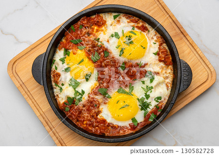 Shakshuka in cast iron skillet with tomatoes, herbs, and sunny-side-up eggs 130582728