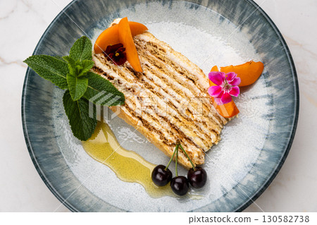 Layered honey cake slice with mint, cherries, and apricot on ceramic plate 130582738