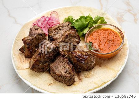 Traditional Georgian grilled meat (mtsvadi) with onion, herbs, and sauce on lavash 130582740