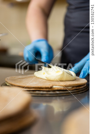 Spreading creamy custard on a cake layer in a professional bakery kitchen Spreading creamy custard on a cake layer in a professional bakery kitchen 130582741