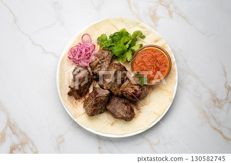 Traditional Georgian grilled meat (mtsvadi) with onion, herbs, and sauce on lavash 130582745
