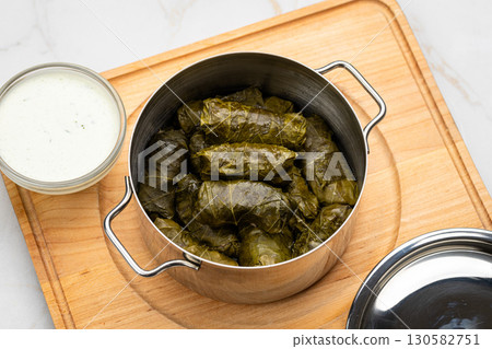 Stuffed grape leaves called dolma in steel pot with yogurt sauce on wooden board Stuffed grape leaves called dolma in steel pot with yogurt sauce on wooden board 130582751