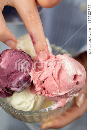 Finger touching creamy mixed ice cream scoops in glass bowl close-up, pastel tones Finger touching creamy mixed ice cream scoops in glass bowl close-up, pastel tones 130582763