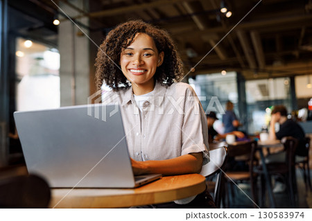 A Young Woman Focused on Her Work While Using a Laptop in a Trendy and Modern Cafe Ambiance 130583974