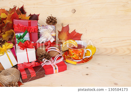 Thanksgiving, autumn background with seasonal maple leaves, a cup of hot tea with lemon and gifts on a wooden background, copy space, preparation for the holiday. Happy Thanksgiving concept, 130584173