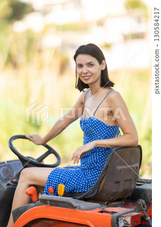 Young woman sits on minitractor and drives rural vehicle, performs loading work on farm 130584217